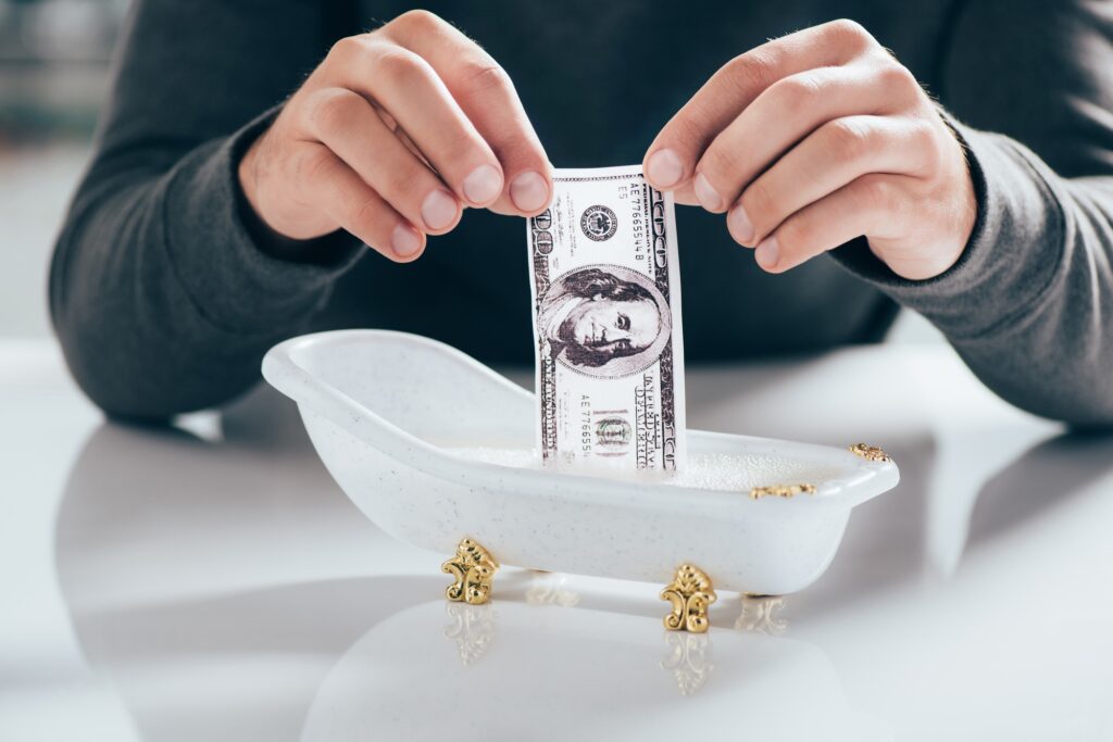 cropped shot of man washing dollar banknote in small bathtub, money laundering concept